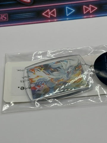 A clear acrylic keychain featuring an Reshiram character illustration, sealed in a transparent plastic bag with a white card insert and a black tag, photographed on a light surface.