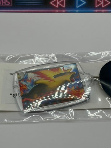 A Pokémon keychain featuring a shiny, iridescent Typhlosion card inside a clear plastic sleeve, resting on a white surface.