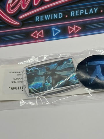 Zekrom keyring, with sticker, placed on a white surface in front of a neon-style sign that reads 'REWIND REPLAY'.