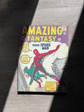 A Amazing Fantasy #15 Spider-Man comic book canvas art lying on a gray wood floor, partially shaded by a strong diagonal shadow. The comic cover features Spider-Man in red and blue swinging from a building, with the title 'AMAZING FANTASY' in large yellow letters at the bottom.