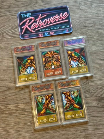 Five Yu-Gi-Oh! trading cards in protective plastic cases arranged on a wood floor, with a blue and pink 'The Retroverse' sign above them.