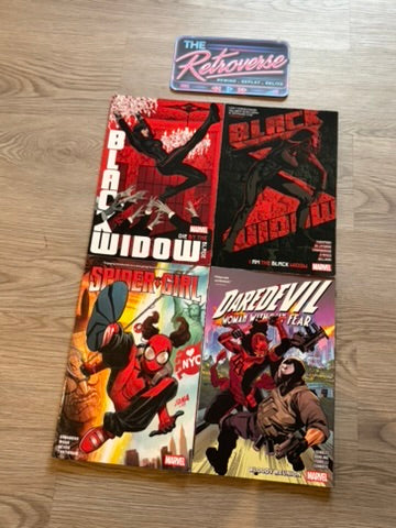 Four Marvel comic books laid out on a light wood floor: Black Widow, Spider-Gwen, Daredevil, and The Retroverse sticker/card above them.