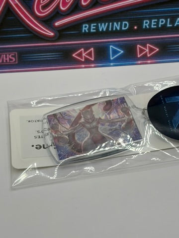 A Pokemon Mewtwo Keyring shown inside a clear plastic sleeve with a white card insert and a dark round tag, placed on a white surface below a neon-style media control sign.