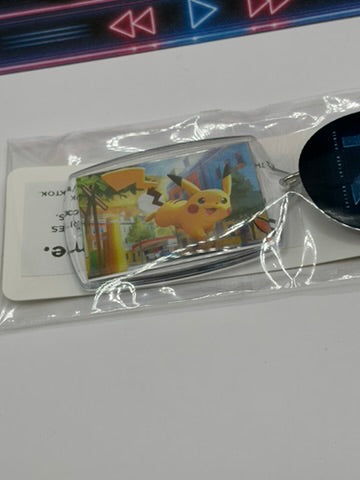 A Pokémon Pikachu acrylic keychain in its clear plastic packaging, featuring a printed illustration of Pikachu on a silver-toned rectangular case with a black metal keyring.