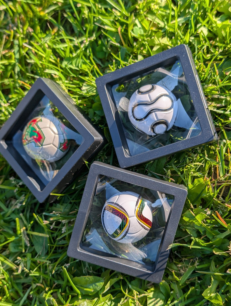 Three miniature soccer balls in display cases on grass