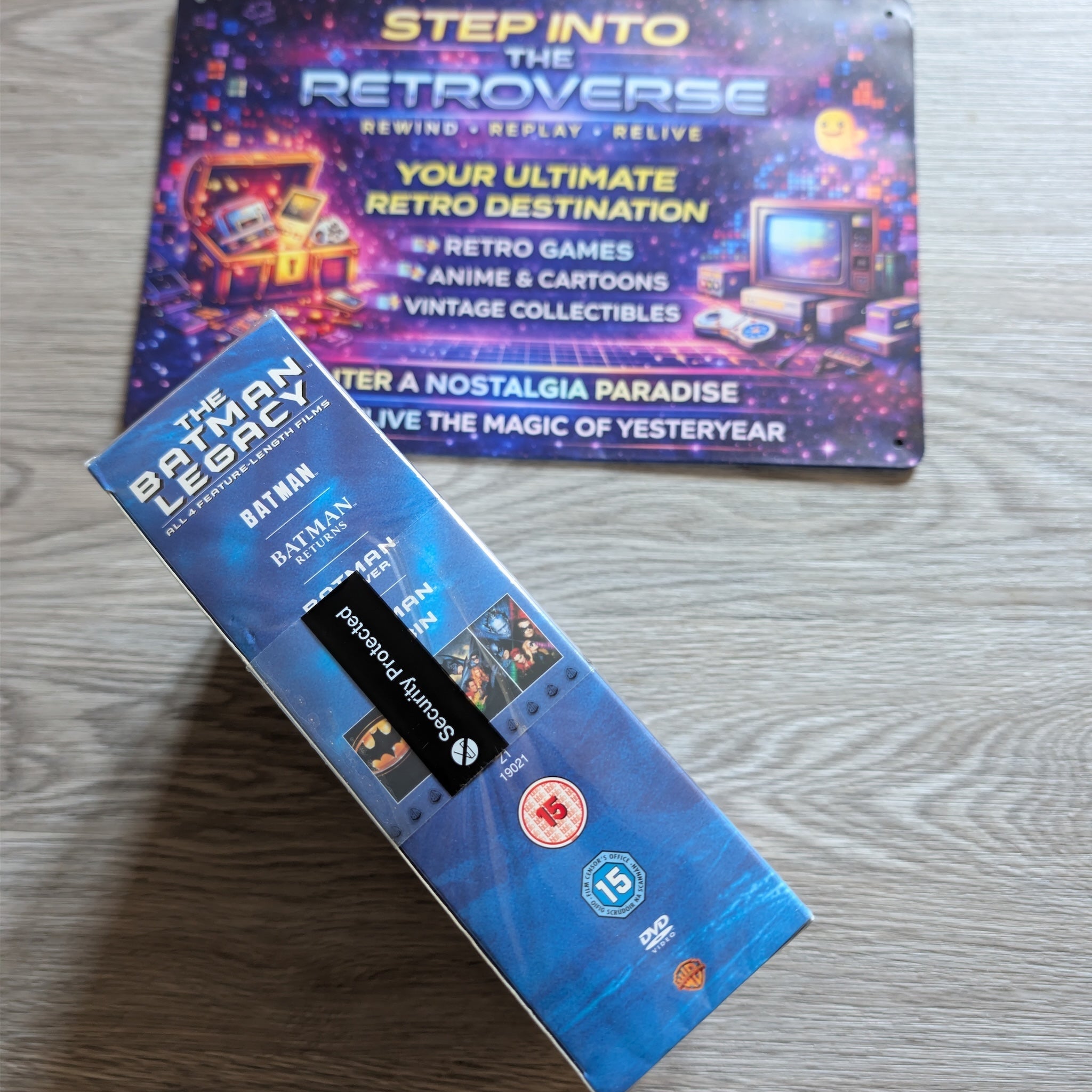 Two product boxes on a wooden surface, one titled 'The Batman Legacy' and the other 'Step into the Retroverse'.