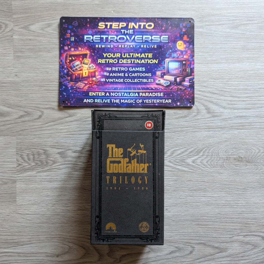 Two video game cases on a wooden surface, one for 'The Godfather Trilogy' and the other for 'Step into the Retroverse'.